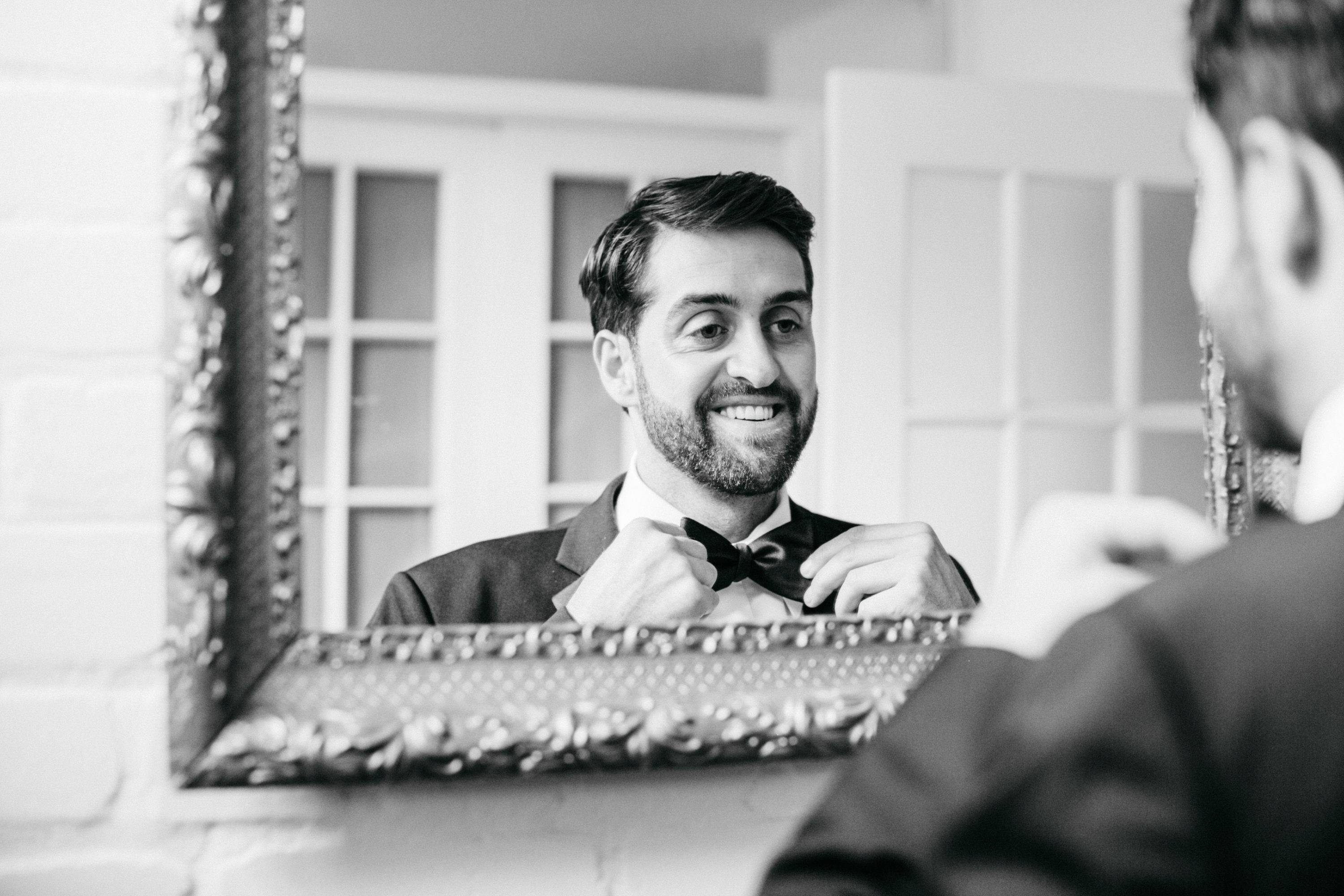 Groom fixing tie in mirror