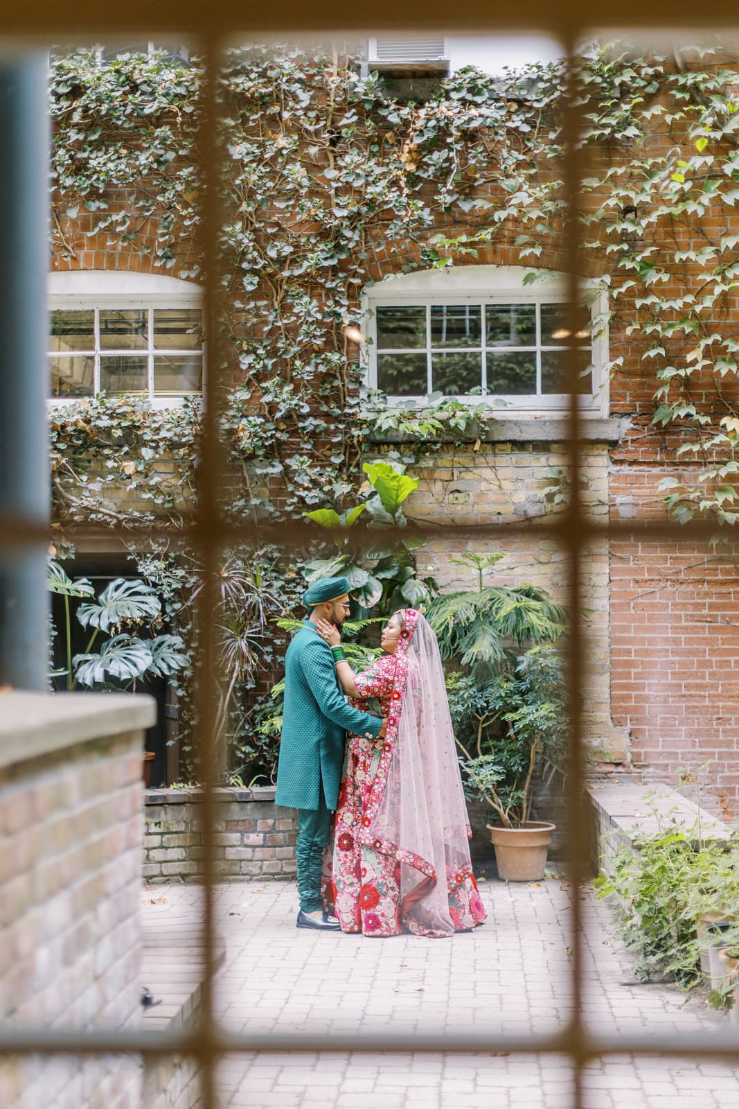 Photo of a bride and groom in Indian attire through steel framed windows